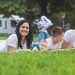 Happy family lying on grass with RV in the background, enjoying a sunny outdoor picnic.