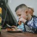 Young boy savoring a grilled chicken meal during an outdoor barbecue.